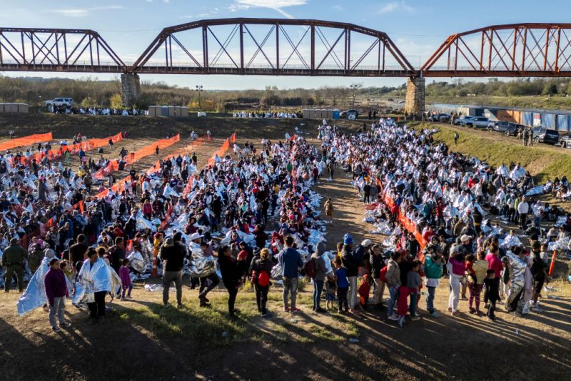 EAGLE PASS, TEXAS - DECEMBER 19: In an aerial view, thousands of immigrants, most wearing thermal blankets, await processing at a U.S. Border Patrol transit center on December 19, 2023 in Eagle Pass, Texas. Major surges of migrants illegally crossing the Rio Grande have overwhelmed U.S. border authorities in recent weeks. (Photo by John Moore/Getty Images)