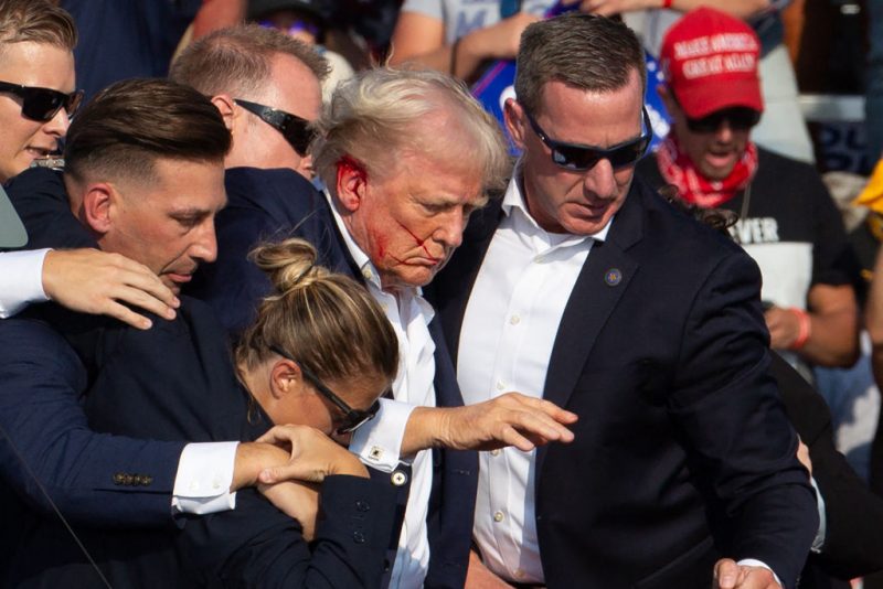 US Republican candidate Donald Trump is seen with blood on his face surrounded by secret service agents as he is taken off the stage at a campaign event at Butler Farm Show Inc. in Butler, Pennsylvania, on July 13, 2024. Trump was hit in the ear in an apparent assassination attempt by a gunman at a campaign rally on Saturday, in a chaotic and shocking incident that will fuel fears of instability ahead of the 2024 US presidential election. The 78-year-old former president was rushed off stage with blood smeared across his face after the shooting in Butler, Pennsylvania, while the gunman and a bystander were killed and two spectators critically injured. (Photo by Rebecca DROKE / AFP) / QUALITY REPEAT (Photo by REBECCA DROKE/AFP via Getty Images)