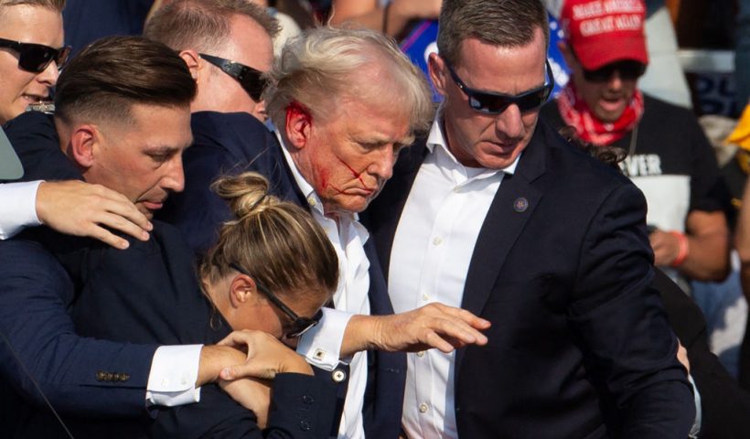 US Republican candidate Donald Trump is seen with blood on his face surrounded by secret service agents as he is taken off the stage at a campaign event at Butler Farm Show Inc. in Butler, Pennsylvania, on July 13, 2024. Trump was hit in the ear in an apparent assassination attempt by a gunman at a campaign rally on Saturday, in a chaotic and shocking incident that will fuel fears of instability ahead of the 2024 US presidential election. The 78-year-old former president was rushed off stage with blood smeared across his face after the shooting in Butler, Pennsylvania, while the gunman and a bystander were killed and two spectators critically injured. (Photo by Rebecca DROKE / AFP) / QUALITY REPEAT (Photo by REBECCA DROKE/AFP via Getty Images)