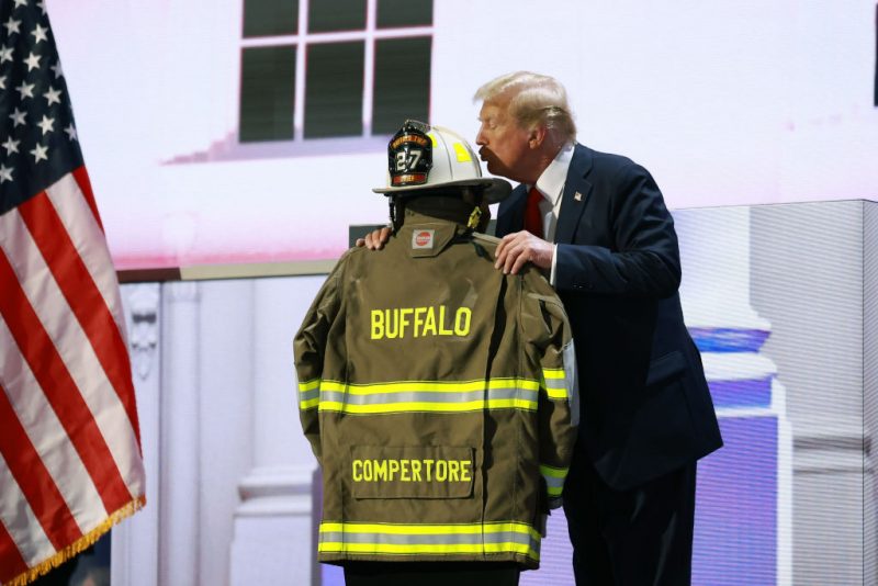 MILWAUKEE, WISCONSIN - JULY 18: Republican presidential nominee, former U.S. President Donald Trump embraces the firefighter uniform of Corey Comperatore as he speaks on stage on the fourth day of the Republican National Convention at the Fiserv Forum on July 18, 2024 in Milwaukee, Wisconsin. Delegates, politicians, and the Republican faithful are in Milwaukee for the annual convention, concluding with former President Donald Trump accepting his party's presidential nomination. The RNC takes place from July 15-18. (Photo by Joe Raedle/Getty Images)