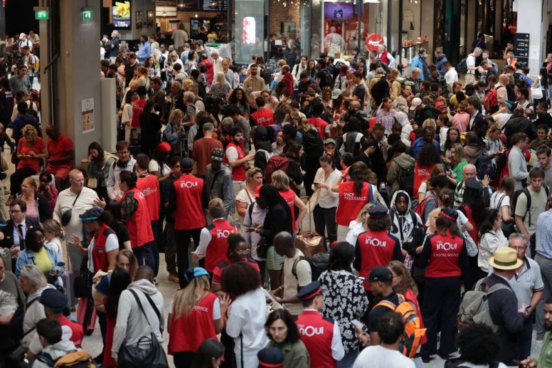 TOPSHOT - Employees of SNCF railway company speak to passengers waiting for their trains' departure at the Gare Montparnasse train station in Paris on July 26, 2024 as France's high-speed rail network was hit by malicious acts disrupting the transport system hours before the opening ceremony of the Paris 2024 Olympic Games. According to SNCF a massive attack on a large scale hit the TGV network and many routes will have to be cancelled. SNCF urged passengers to postpone their trips and stay away from train stations. (Photo by Thibaud MORITZ / AFP) (Photo by THIBAUD MORITZ/AFP via Getty Images)