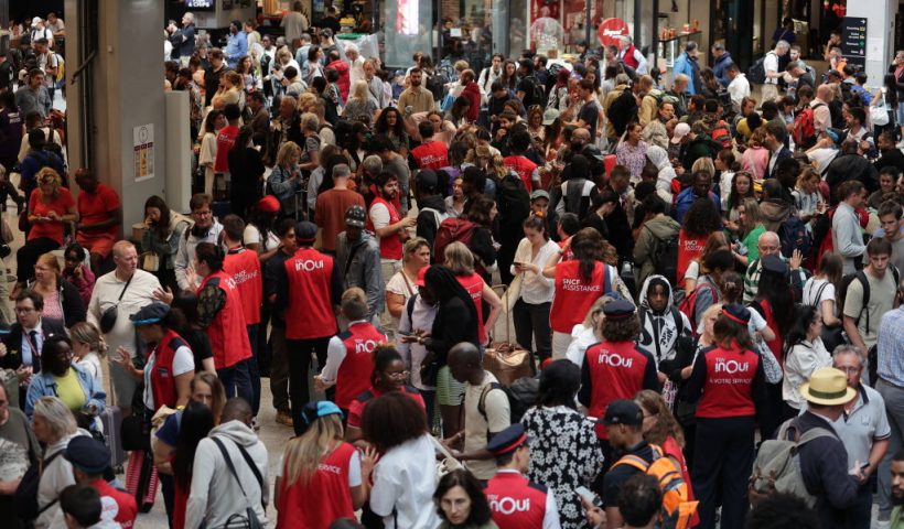 TOPSHOT - Employees of SNCF railway company speak to passengers waiting for their trains' departure at the Gare Montparnasse train station in Paris on July 26, 2024 as France's high-speed rail network was hit by malicious acts disrupting the transport system hours before the opening ceremony of the Paris 2024 Olympic Games. According to SNCF a massive attack on a large scale hit the TGV network and many routes will have to be cancelled. SNCF urged passengers to postpone their trips and stay away from train stations. (Photo by Thibaud MORITZ / AFP) (Photo by THIBAUD MORITZ/AFP via Getty Images)