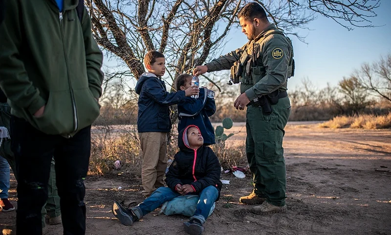 A Border Patrol agent gives a group of unaccompanied minors water after they were apprehended near the highway on February 4, 2024 outside Eagle Pass, Texas. Eagle Pass, about 20 miles (30 kilometers) from Quemado, has become the epicenter of a prickly conflict between Texas Governor Greg Abbott, a Republican, and the Biden administration. The federal government is suing Abbott for taking control of Shelby Park that includes an access ramp to the river, and for laying barbed wire along the riverbank. (Photo by SERGIO FLORES / AFP) (Photo by SERGIO FLORES/AFP via Getty Images)