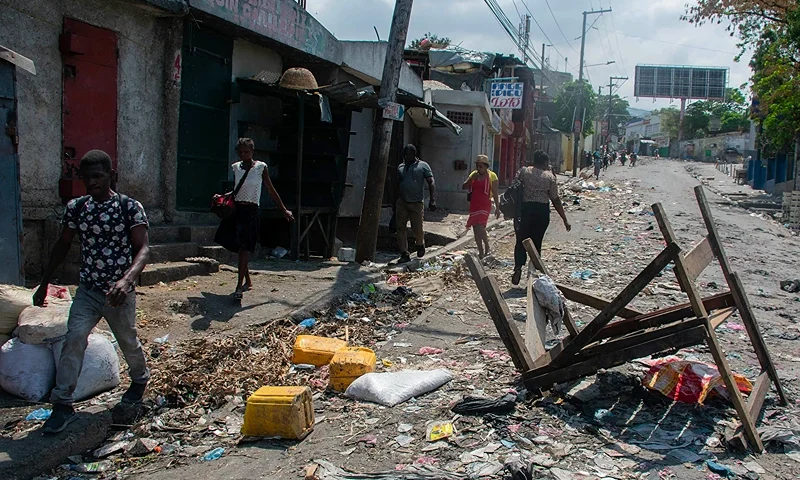 TOPSHOT - People walk past a barricade in a road in Port-au-Prince, Haiti, on March 20, 2024. Negotiations to form a transitional council to govern Haiti advanced on March 20, as the United States airlifted more citizens to safety from gang violence that has plunged the impoverished country into chaos. (Photo by Clarens SIFFROY / AFP) (Photo by CLARENS SIFFROY/AFP via Getty Images)