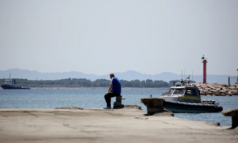 A man watches as a speed boat of Italian law enforcement agency Guardia di Finanza (GdF) is navigated near the site of a recently build Italian-run migrant centre at the port of Shengjin, some 60 kms northwest of Tirana, on June 5, 2024. The controversial deal to host two holding centres for migrants rescued in Italian water, approved by Albania's parliament on February 2024 and regularly denounced by opposition parties in both countries as well as by rights groups, allows for two centres to be built near the Albanian port of Shengjin, where migrants would register for asylum, as well as a facility in the same region to house those awaiting a response to their applications. (Photo by Adnan Beci / AFP) (Photo by ADNAN BECI/AFP via Getty Images)