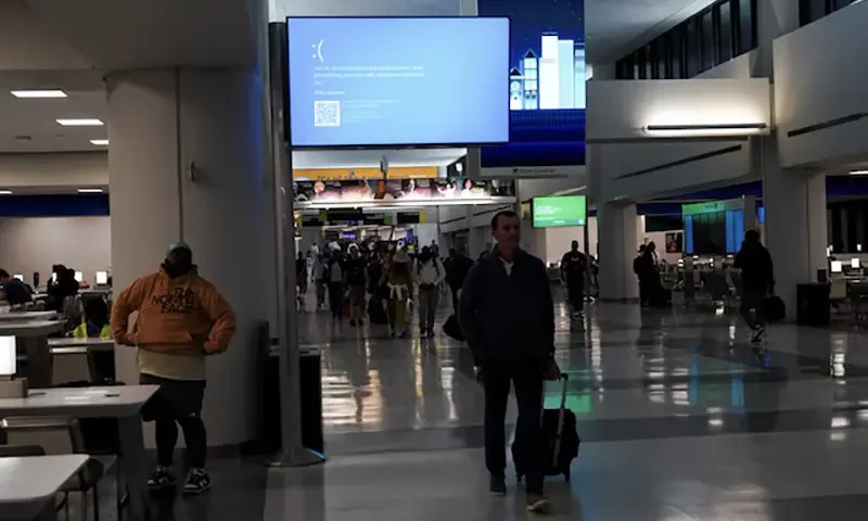 Travelers walk past a monitor displaying a blue error screen, also known as the "Blue Screen of Death" inside Terminal C in Newark International Airport, after a worldwide tech outage caused by an update to Crowdstrike's "Falcon Sensor" software which crashed Microsoft Windows systems, in Newark, New Jersey, U.S., July 19, 2024. REUTERS/Bing Guan/File Photo