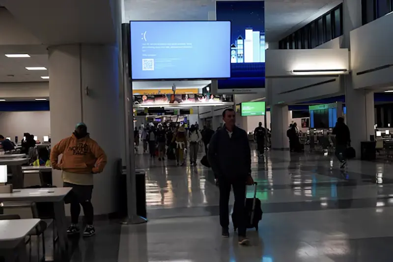 Travelers walk past a monitor displaying a blue error screen, also known as the "Blue Screen of Death" inside Terminal C in Newark International Airport, after a worldwide tech outage caused by an update to Crowdstrike's "Falcon Sensor" software which crashed Microsoft Windows systems, in Newark, New Jersey, U.S., July 19, 2024. REUTERS/Bing Guan/File Photo