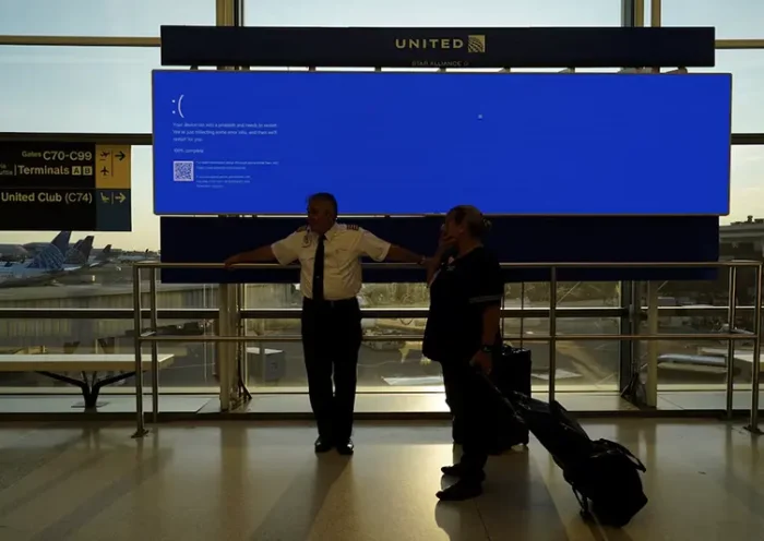 United Airlines employees wait by a departures monitor displaying a blue error screen, also known as the “Blue Screen of Death” inside Terminal C in Newark International Airport, after United Airlines and other airlines grounded flights due to a worldwide tech outage caused by an update to CrowdStrike's "Falcon Sensor" software which crashed Microsoft Windows systems, in Newark, New Jersey, U.S., July 19, 2024. REUTERS/Bing Guan/File Photo