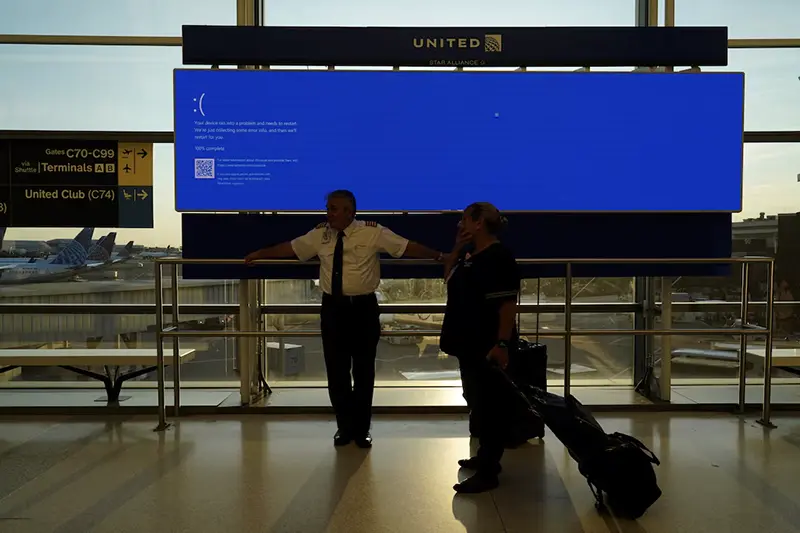 United Airlines employees wait by a departures monitor displaying a blue error screen, also known as the “Blue Screen of Death” inside Terminal C in Newark International Airport, after United Airlines and other airlines grounded flights due to a worldwide tech outage caused by an update to CrowdStrike's "Falcon Sensor" software which crashed Microsoft Windows systems, in Newark, New Jersey, U.S., July 19, 2024. REUTERS/Bing Guan/File Photo