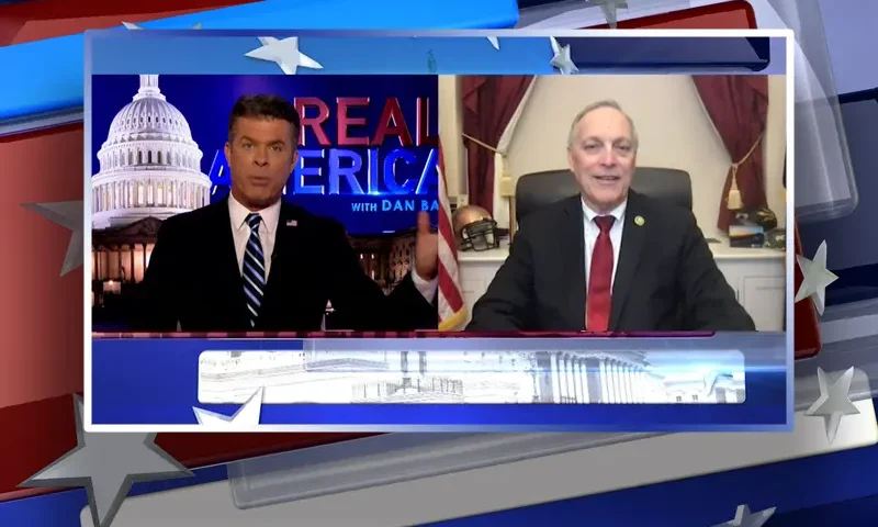 Video still from Real America on One America News Network showing a split screen of the host on the left side, and on the right side is the guest, Andy Biggs.