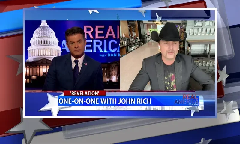 Video still from Real America on One America News Network showing a split screen of the host on the left side, and on the right side is the guest, John Rich.