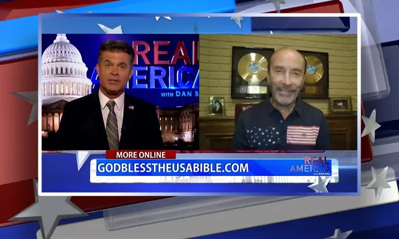 Video still from Real America on One America News Network showing a split screen of the host on the left side, and on the right side is the guest, Lee Greenwood.