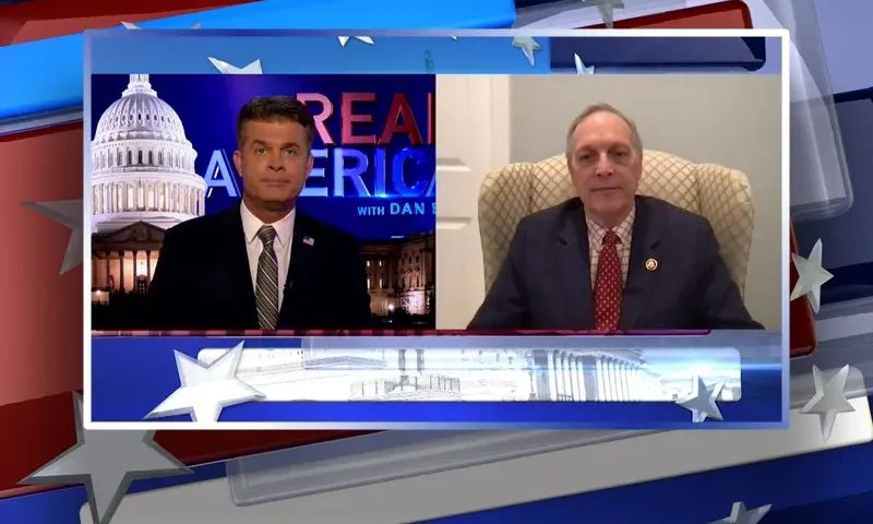 Video still from Real America on One America News Network showing a split screen of the host on the left side, and on the right side is the guest, Rep. Andy Biggs.